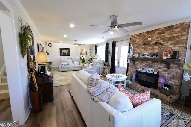 living room featuring ceiling fan, wood-type flooring, a brick fireplace, and ornamental molding