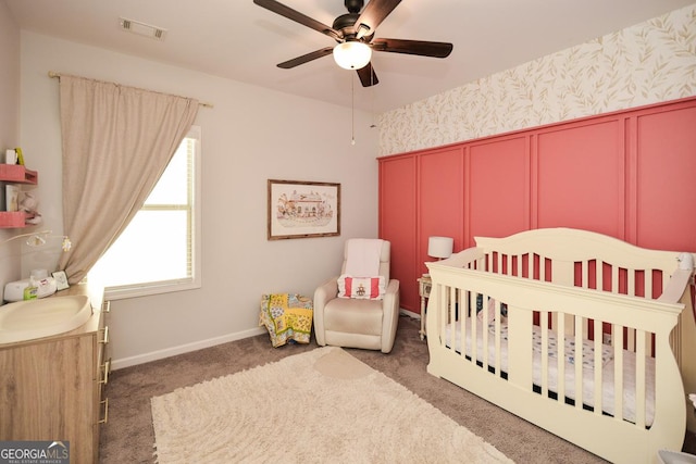 bedroom featuring dark carpet, ceiling fan, and a nursery area