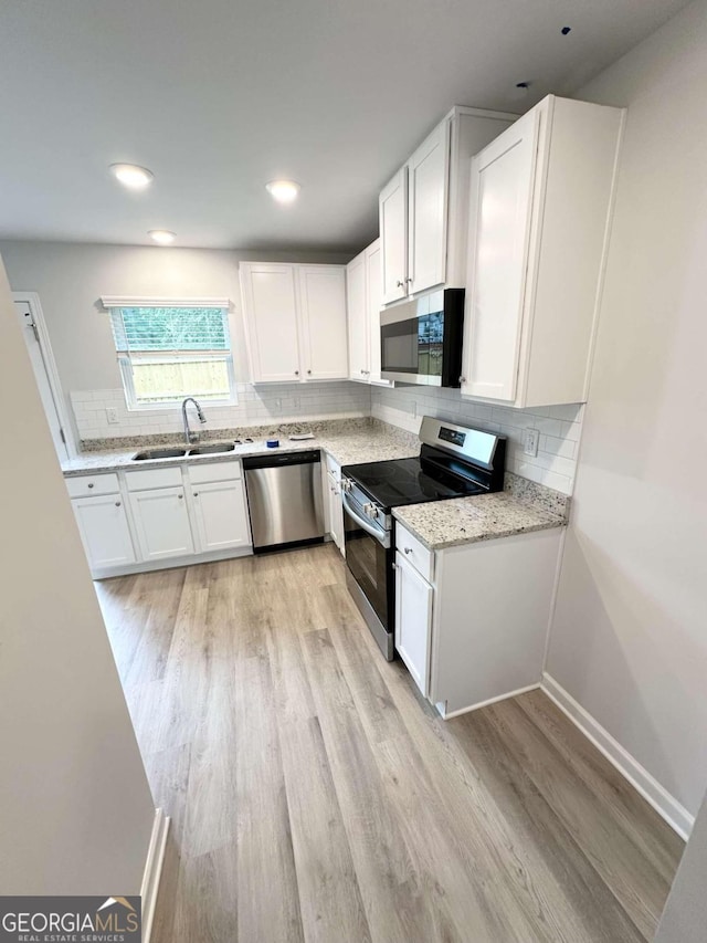 kitchen with sink, white cabinetry, light wood-type flooring, appliances with stainless steel finishes, and light stone counters