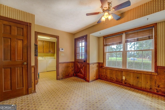 unfurnished room with ceiling fan, a healthy amount of sunlight, washer and dryer, and wood walls