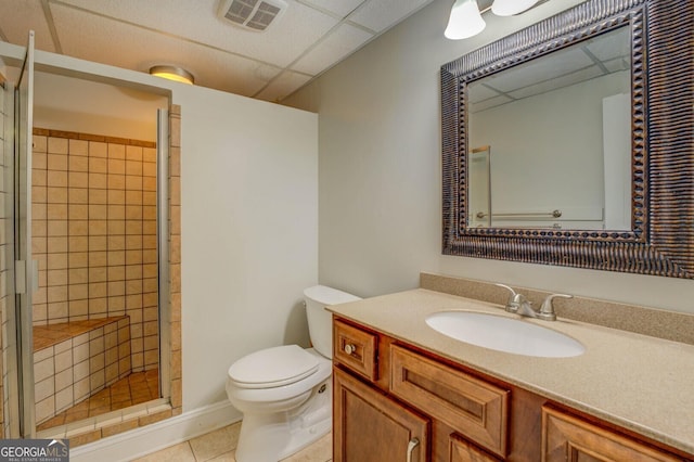 bathroom with tile patterned flooring, tiled shower, vanity, a drop ceiling, and toilet