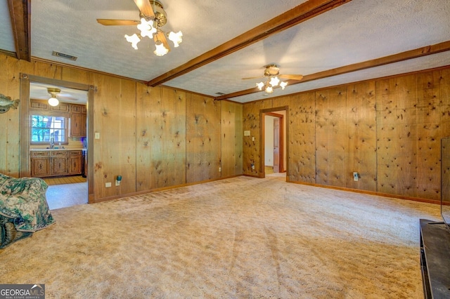 carpeted empty room with beamed ceiling, sink, a textured ceiling, and wood walls