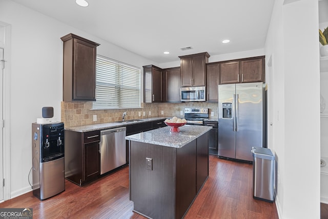 kitchen with light stone countertops, dark brown cabinets, stainless steel appliances, and a kitchen island