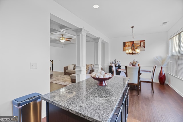 kitchen with ceiling fan with notable chandelier, light stone countertops, a kitchen island, ornate columns, and hanging light fixtures