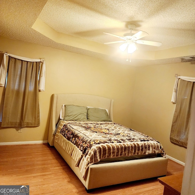 bedroom featuring a raised ceiling, ceiling fan, a textured ceiling, and light hardwood / wood-style floors