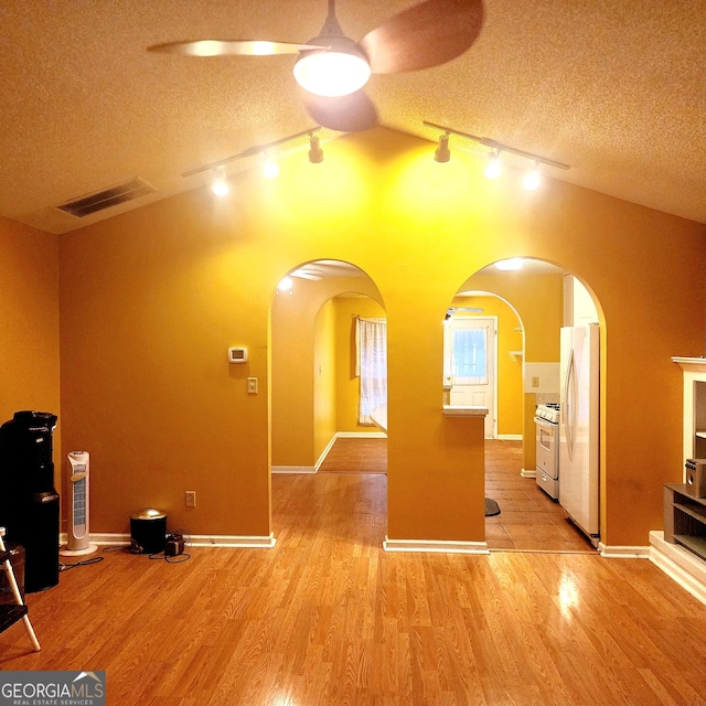 interior space featuring ceiling fan, a textured ceiling, lofted ceiling, and light wood-type flooring