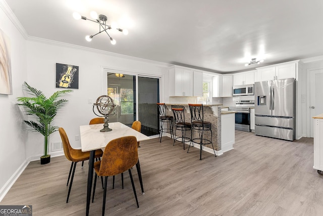 dining area with light hardwood / wood-style flooring, crown molding, and an inviting chandelier