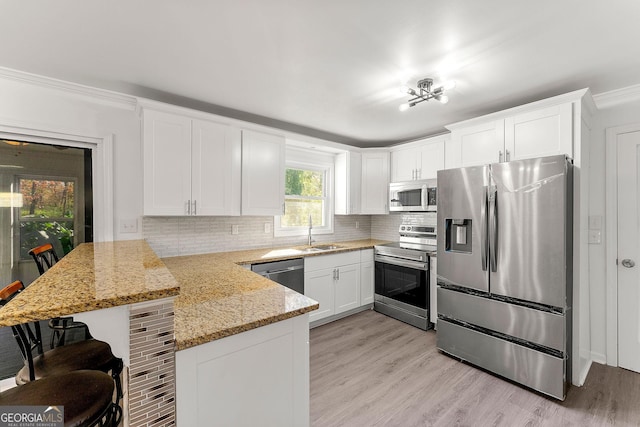 kitchen featuring white cabinets, stainless steel appliances, kitchen peninsula, light stone counters, and a breakfast bar