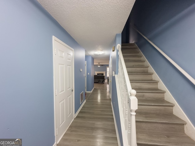 staircase with visible vents, baseboards, a textured ceiling, and wood finished floors