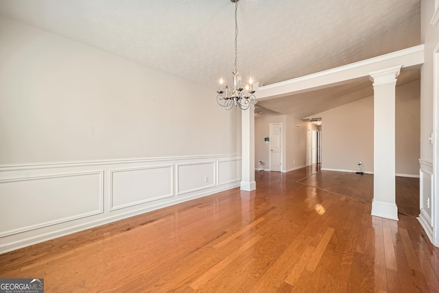 unfurnished dining area with a textured ceiling, an inviting chandelier, wood finished floors, and ornate columns