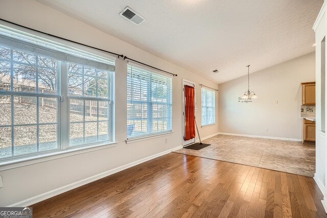 unfurnished dining area featuring wood-type flooring, lofted ceiling, and a chandelier