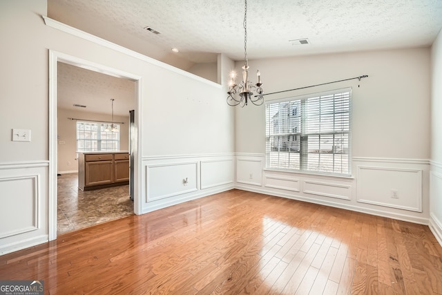 unfurnished dining area featuring visible vents, hardwood / wood-style floors, vaulted ceiling, a textured ceiling, and a notable chandelier