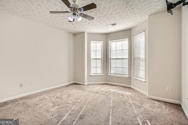 spare room featuring a textured ceiling, a ceiling fan, visible vents, baseboards, and carpet