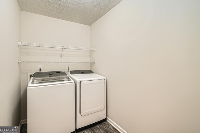 clothes washing area with dark wood-type flooring, washing machine and dryer, a textured ceiling, laundry area, and baseboards