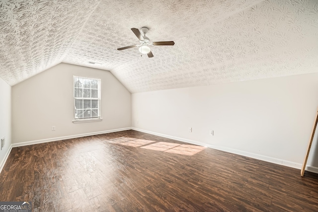 additional living space featuring a textured ceiling, lofted ceiling, dark wood-type flooring, a ceiling fan, and baseboards