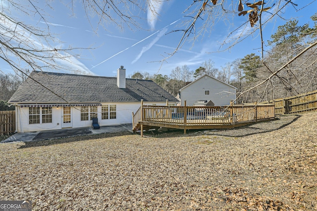 back of house with a patio, a fenced backyard, roof with shingles, a wooden deck, and a chimney