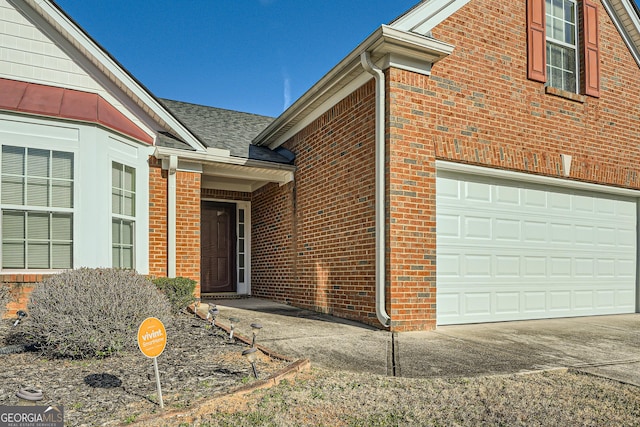 doorway to property with a garage, concrete driveway, brick siding, and roof with shingles