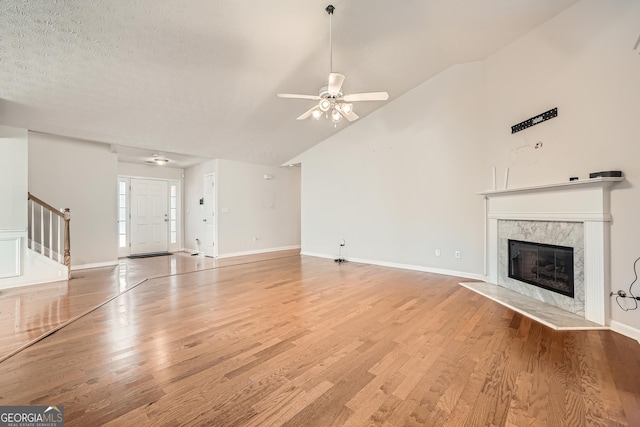 unfurnished living room featuring a textured ceiling, vaulted ceiling, a premium fireplace, light wood-type flooring, and ceiling fan