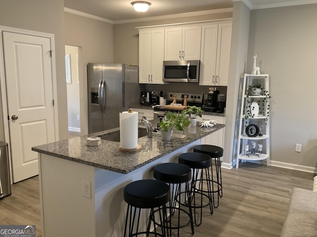 kitchen featuring white cabinetry, appliances with stainless steel finishes, a breakfast bar area, and an island with sink