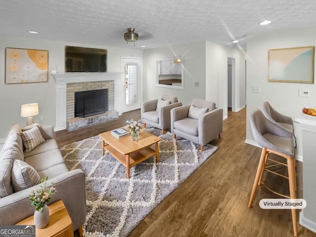 living room with a textured ceiling, ceiling fan, a fireplace, and hardwood / wood-style floors