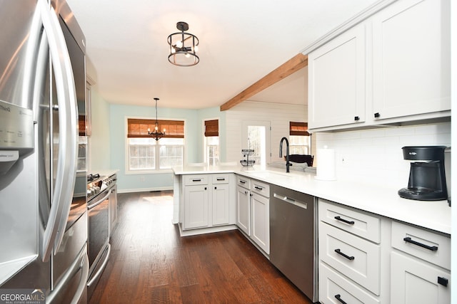 kitchen with appliances with stainless steel finishes, white cabinetry, hanging light fixtures, kitchen peninsula, and a notable chandelier