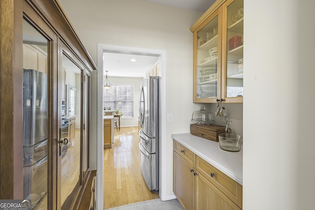 kitchen with stainless steel fridge, decorative light fixtures, and light hardwood / wood-style floors