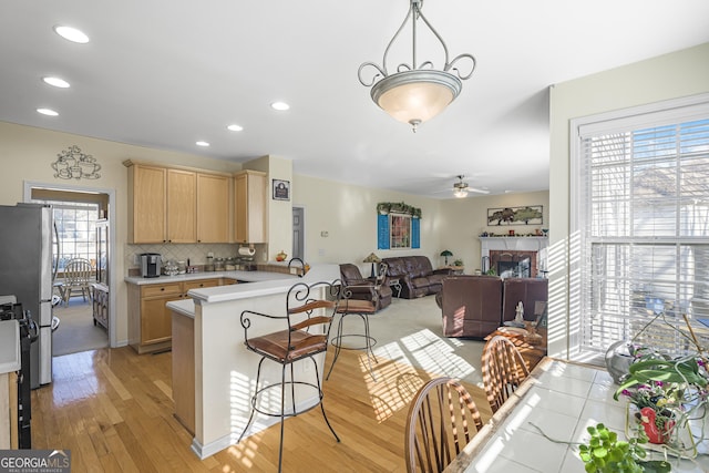 kitchen featuring light brown cabinetry, kitchen peninsula, stainless steel refrigerator, and a breakfast bar