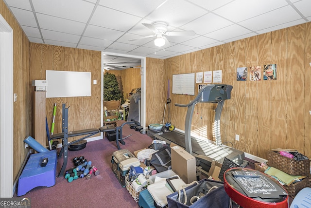 exercise area featuring carpet, a drop ceiling, ceiling fan, and wood walls