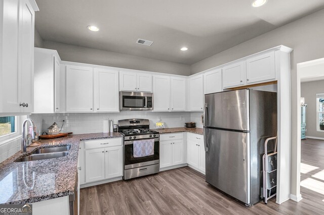 kitchen with white cabinetry, stainless steel appliances, sink, and dark stone counters