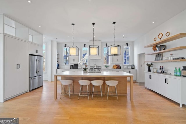 kitchen featuring stainless steel fridge, light countertops, white cabinetry, open shelves, and a sink