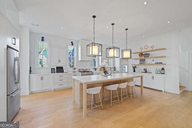 kitchen featuring stainless steel appliances, a breakfast bar, white cabinetry, light wood-style floors, and a center island