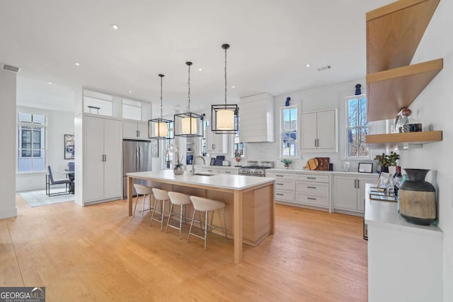 kitchen with decorative light fixtures, white cabinetry, appliances with stainless steel finishes, an island with sink, and a breakfast bar area