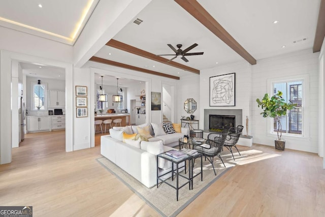 living room featuring ceiling fan, light hardwood / wood-style flooring, and beamed ceiling