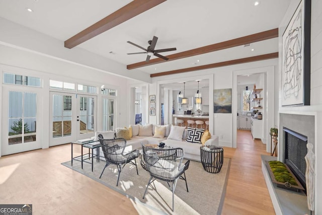 living room featuring ceiling fan, light hardwood / wood-style flooring, beam ceiling, and french doors