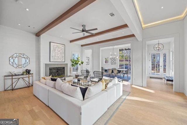 living room with ceiling fan with notable chandelier, light hardwood / wood-style floors, a large fireplace, and beam ceiling