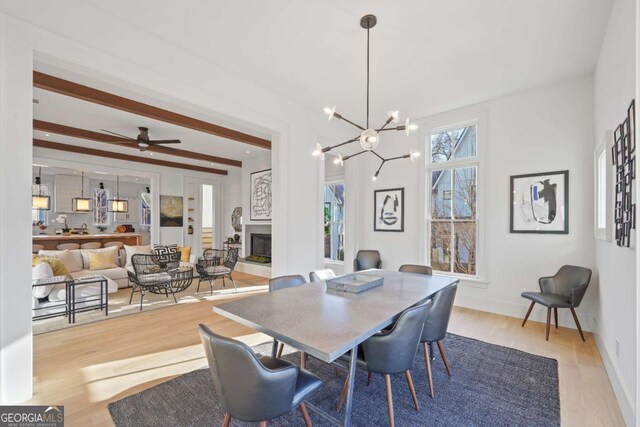 dining space with ceiling fan with notable chandelier, beam ceiling, and light wood-type flooring