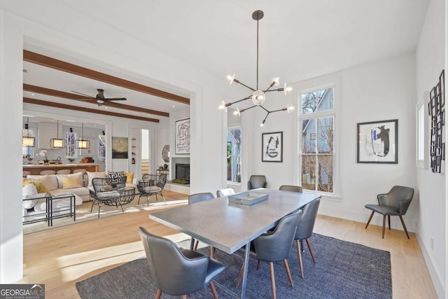 dining room featuring baseboards, a glass covered fireplace, wood finished floors, an inviting chandelier, and beam ceiling