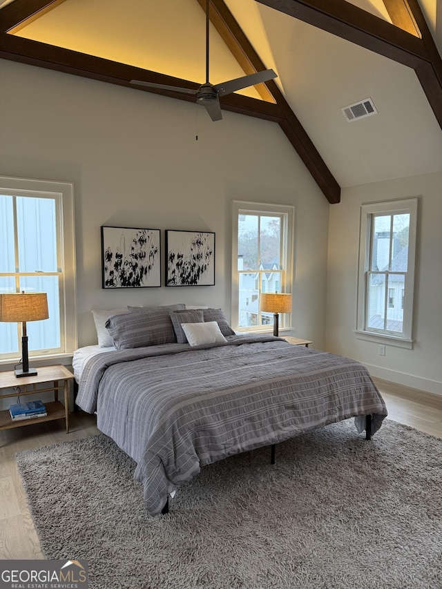 bedroom featuring baseboards, visible vents, beamed ceiling, wood finished floors, and high vaulted ceiling