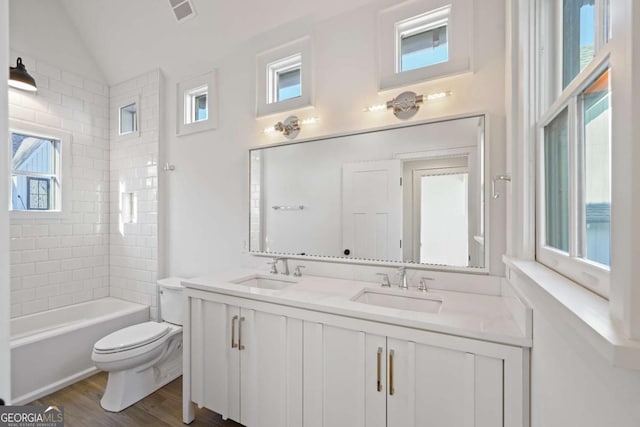 full bathroom featuring hardwood / wood-style floors, lofted ceiling, tiled shower / bath, vanity, and toilet