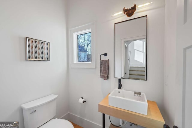 half bath with baseboards, a sink, and toilet