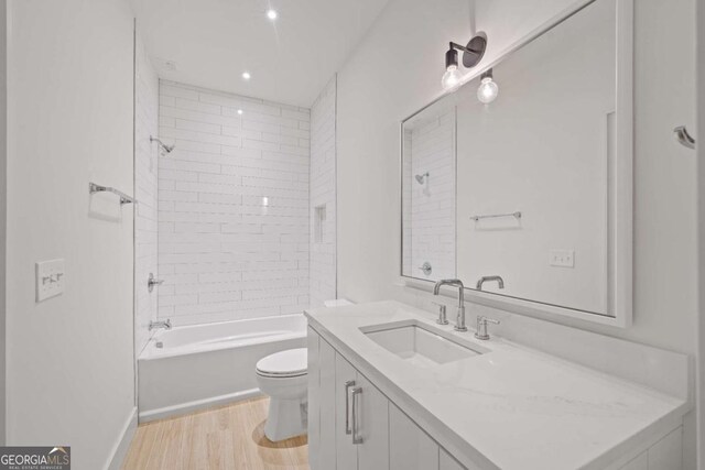 full bathroom with toilet, tiled shower / bath combo, wood-type flooring, and vanity