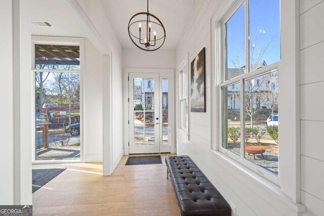 doorway to outside with a wealth of natural light, hardwood / wood-style floors, and a notable chandelier