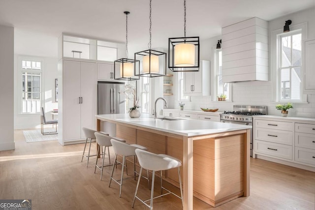 kitchen featuring backsplash, appliances with stainless steel finishes, a kitchen island with sink, light wood-type flooring, and a kitchen breakfast bar