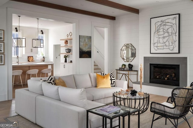 living room with stairs, beam ceiling, a fireplace with raised hearth, and wood finished floors