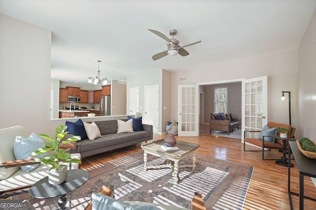 living room with ceiling fan with notable chandelier, light hardwood / wood-style flooring, and french doors