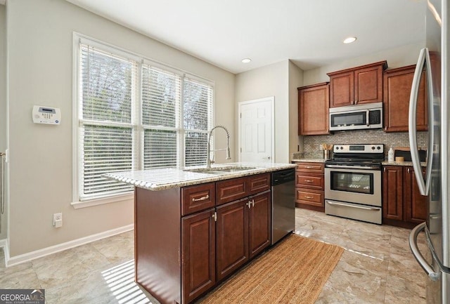 kitchen featuring light stone countertops, stainless steel appliances, tasteful backsplash, sink, and a center island with sink