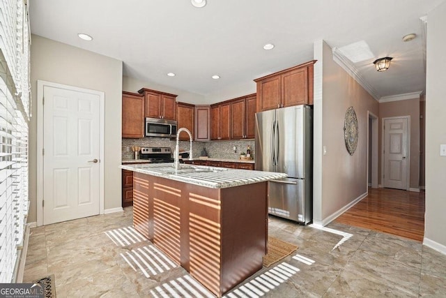 kitchen featuring an island with sink, appliances with stainless steel finishes, backsplash, light stone countertops, and crown molding