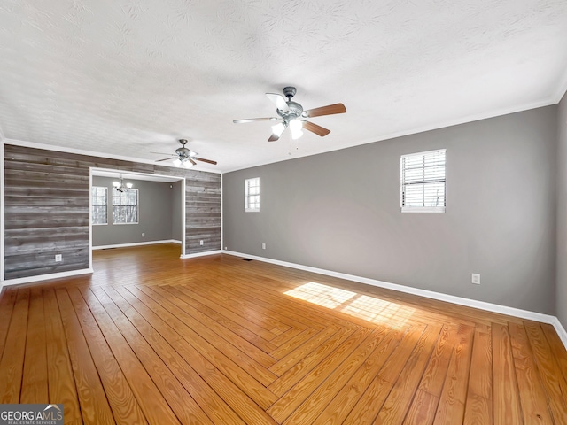 spare room with a textured ceiling, a wealth of natural light, ceiling fan with notable chandelier, and wood walls