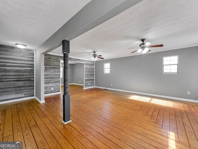 interior space featuring plenty of natural light, a textured ceiling, wood walls, and light wood-type flooring