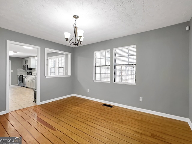 empty room featuring light hardwood / wood-style floors, a textured ceiling, and a chandelier